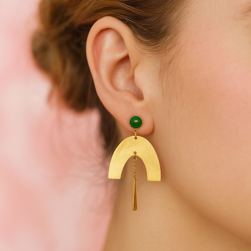 Gold earring with a green gemstone worn by a person against a pink background
