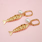 Gold fish-shaped earrings with pearl accents on a pink background