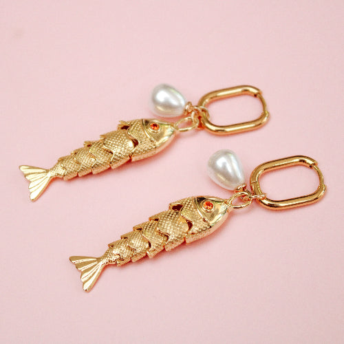 Gold fish-shaped earrings with pearl accents on a pink background