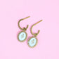 Pair of earrings with snake designs on a pink background