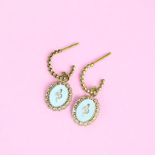 Pair of earrings with snake designs on a pink background