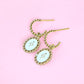 Gold earrings with white stone on a pink background