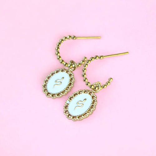 Gold earrings with white stone on a pink background