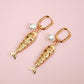 Gold fish-shaped earrings with pearl accents on a pink background