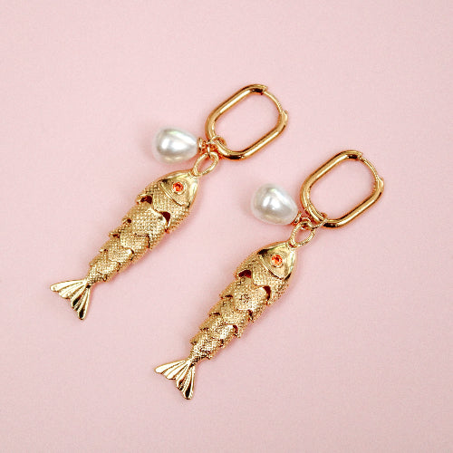 Gold fish-shaped earrings with pearl accents on a pink background